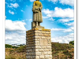 Statue Bigouden en granit surplombant le port de Pors-Poullan, face à l&#039;océan sous un ciel bleu